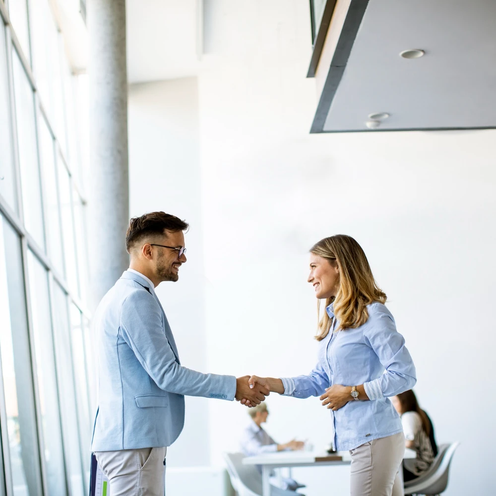 Mann und Frau im Business-Outfit geben sich die Hand in einem modernen Büro – Zeichen für gelungene Zusammenarbeit