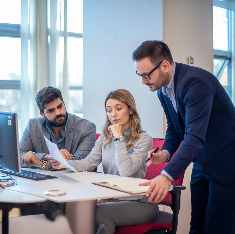 Drei Personen in einem modernen Büro beim gemeinsamen Durchsprechen von Unterlagen vor einem Monitor