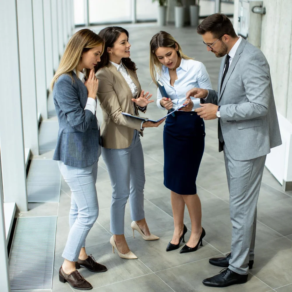 Vier Geschäftspersonen in einem modernen Bürogebäude diskutieren konzentriert über Unterlagen